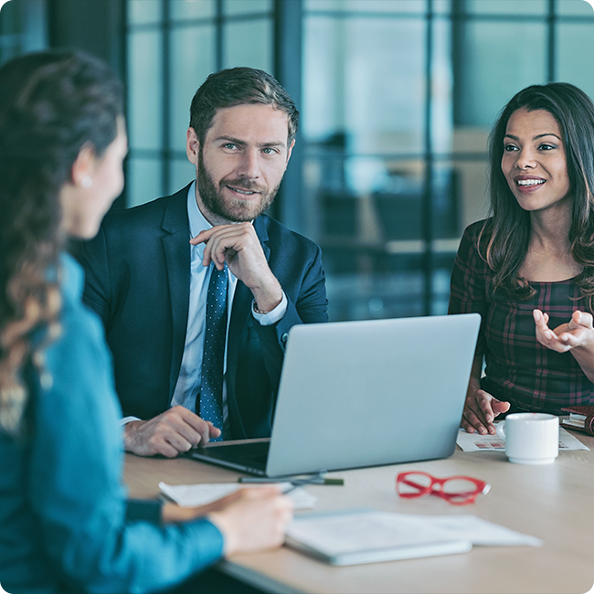 male business professional in a suit in front of a laptop speaking to two female business associates about investment in biotechnology