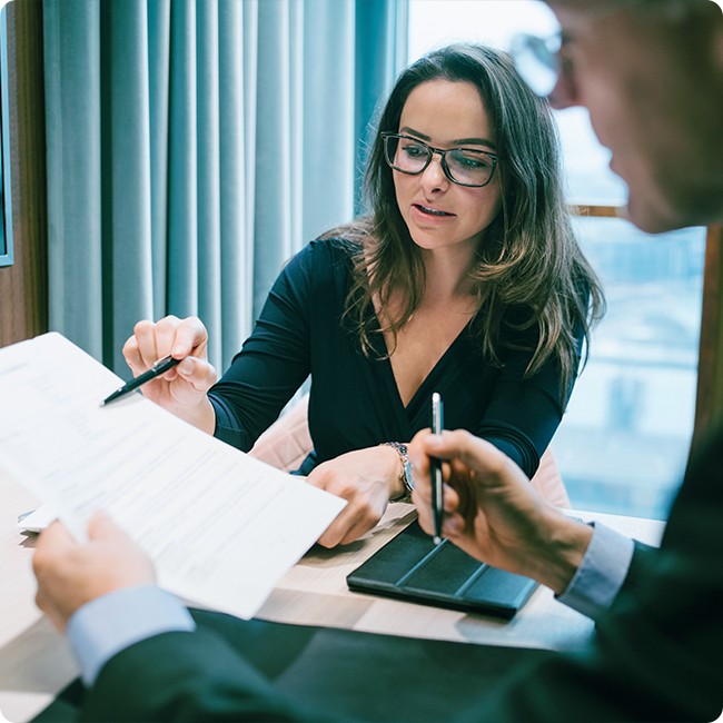 female business professional points at a document with a pen to discuss regulatory and compliance support for biotechnology with a male colleague
