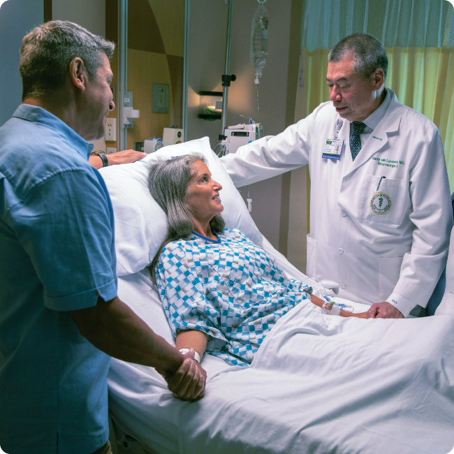 male physician and male visitor at a female patient's bedside in a hospital room