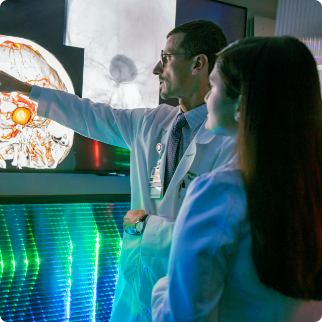 male clinical expert in lab coat showing a medical image to a younger female clinical specialist on a machine in a lab