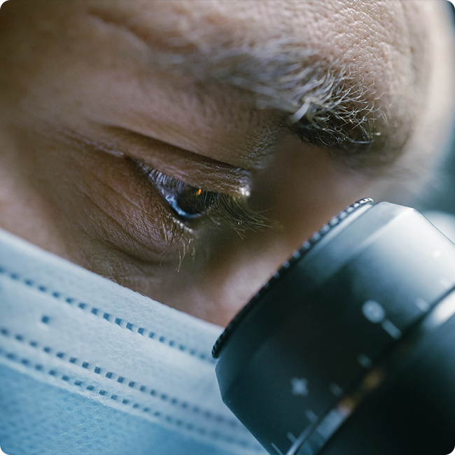 closeup of a male researcher looking through a black microscope